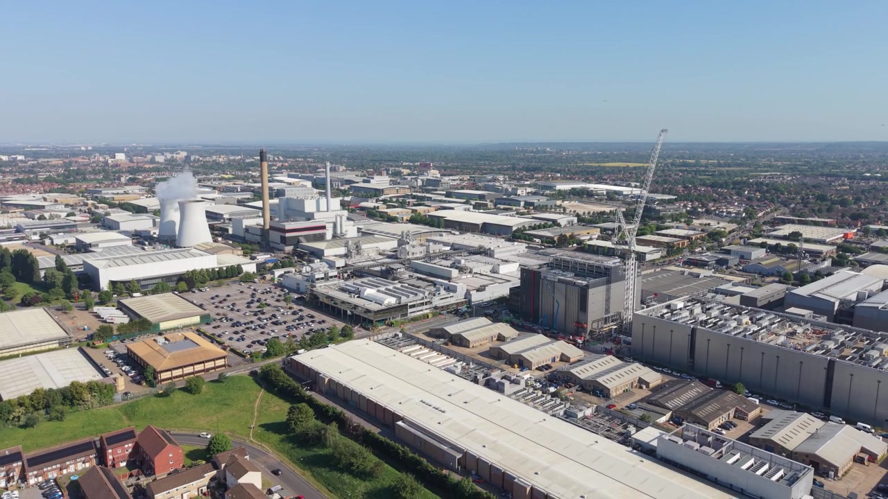 Ampia vista aerea di un grande parco industriale in una giornata di sole splendente. Mostra numerosi data center, una centrale elettrica con una torre di raffreddamento e una gru da costruzione attiva