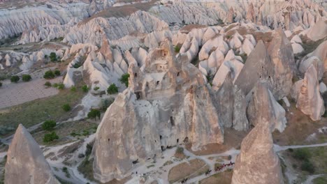 Volando-Lejos-De-La-Iglesia-De-Formación-Rocosa-Con-Caballos-Trotando-A-Lo-Largo-De-Chimeneas-De-Hadas-Que-Revelan-Un-Paisaje-Completo-En-Capadocia,-Turquía