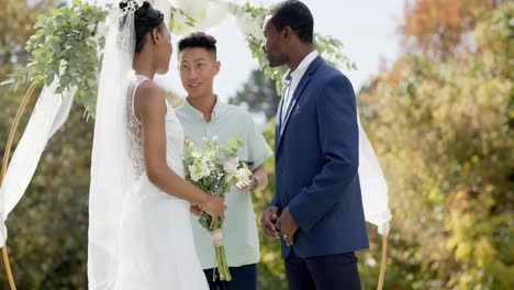 Hombre-Birracial-Oficiando-Ceremonia-De-Boda-Para-Una-Pareja-Afroamericana-En-El-Jardín,-En-Cámara-Lenta