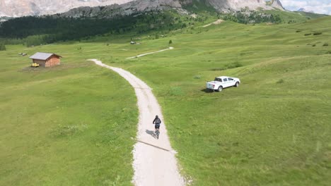 aerial drone tracks mtb cyclist on winding unpaved road in pralongia, italian dolomites