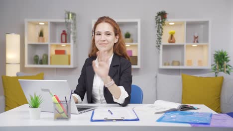 una trabajadora de oficina en casa saludando a la cámara.