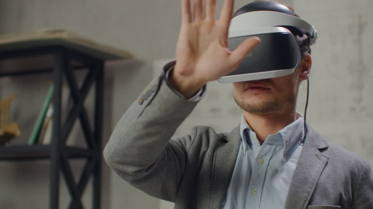 Young man architect in office in virtual reality helmet with hands commits movements simulating a graphic interface work.