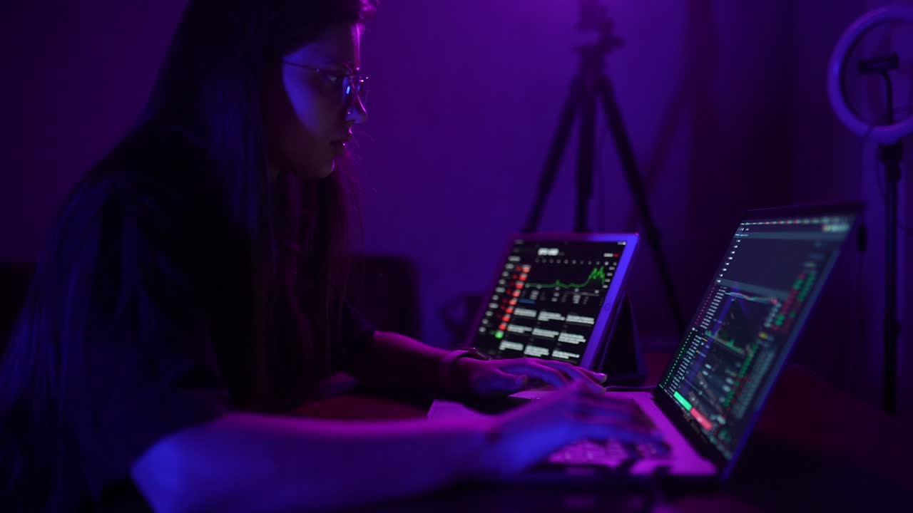 Woman working on laptop at night with financial charts displayed