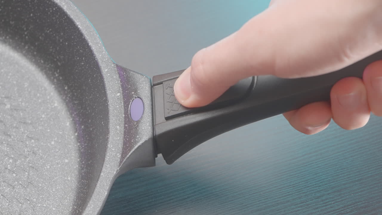 검은색과 회색의 프라이팬 손잡이를 들고 있는 손의 클로즈업