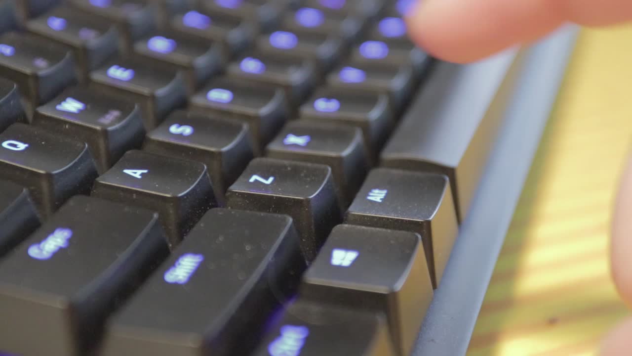 파란색 백라이트 키가 있는 약간 먼지가 많은 검은색 키보드에서 단일 키를 손으로 누르기