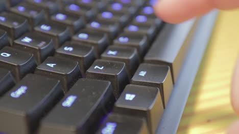 mano presionando una sola tecla en un teclado negro ligeramente polvoriento con teclas retroiluminadas azules