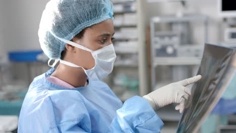 African-american-female-surgeon-looking-at-x-ray-scans-in-operating-theatre,-slow-motion