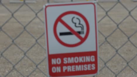 a focus pull red and white no smoking on the premises sign on a chain-linked fence