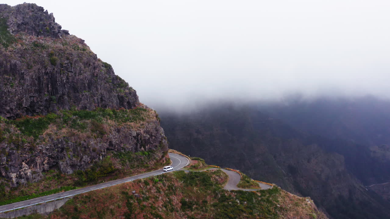 짙은 안개 속에서 산속의 위험한 도로를 달리는 흰색 자동차의 공중 총격