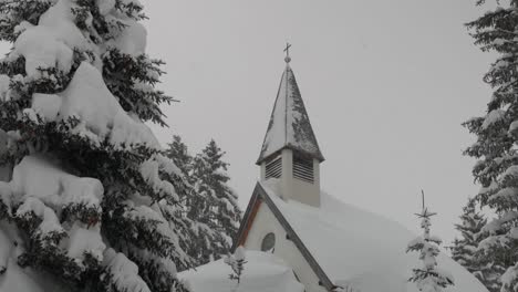 Capilla-Cubierta-De-Nieve-Rodeada-De-árboles,-Tiro-Medio-Inclinado-Hacia-Abajo