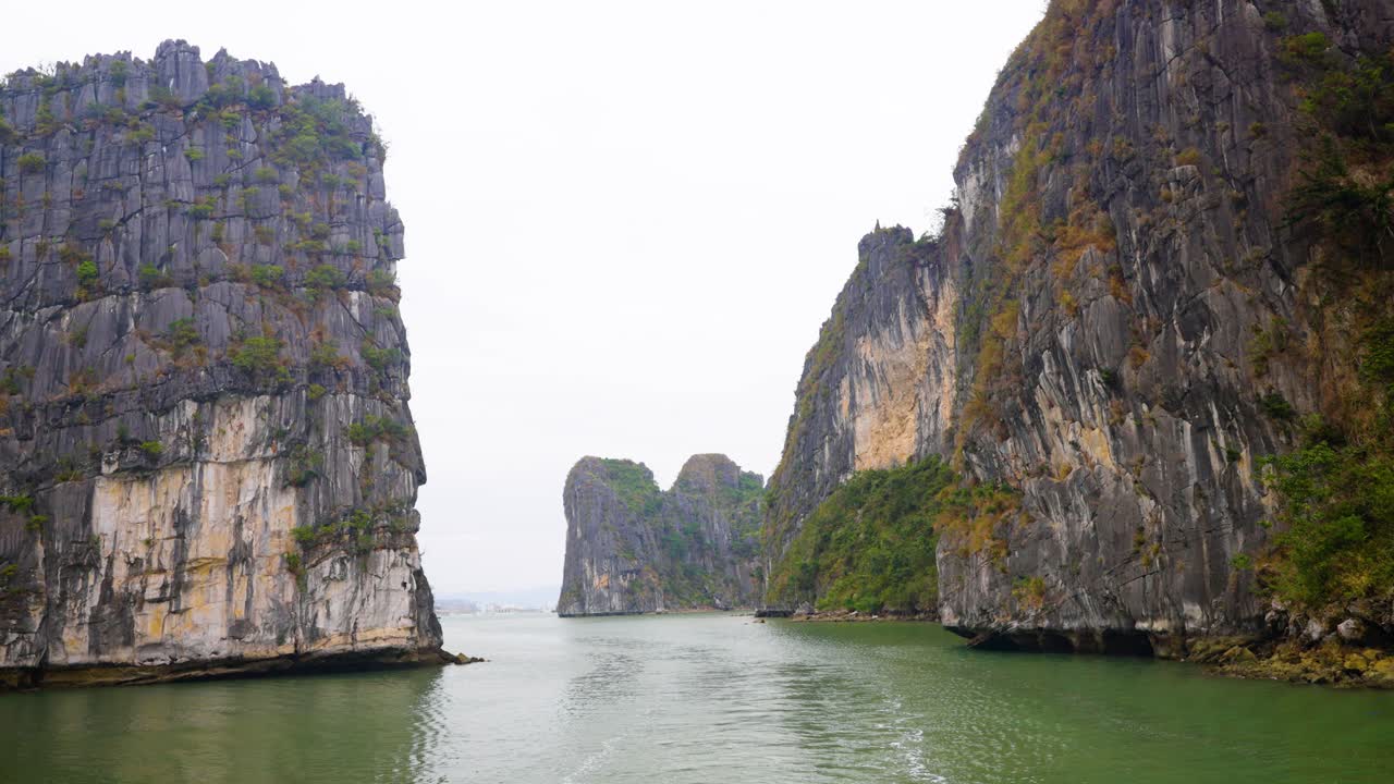 Limestone karsts rise from the emerald waters of Ha Long Bay, cliffs draped in sparse vegetation, creating a mystical seascape that showcases Vietnam most iconic natural wonder