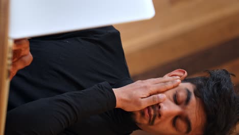 tired and stressed sri lankan man working in front of his laptop, vertical view