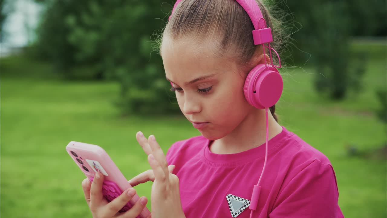 A Young Girl Enjoys Music with Her Pink Headphones While Engaged with Her Device in a Serene Outdoor Setting, Embracing the Joy of Listening