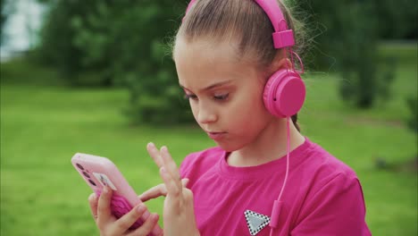 a young girl enjoys music with her pink headphones while engaged with her device in a serene outdoor setting, embracing the joy of listening