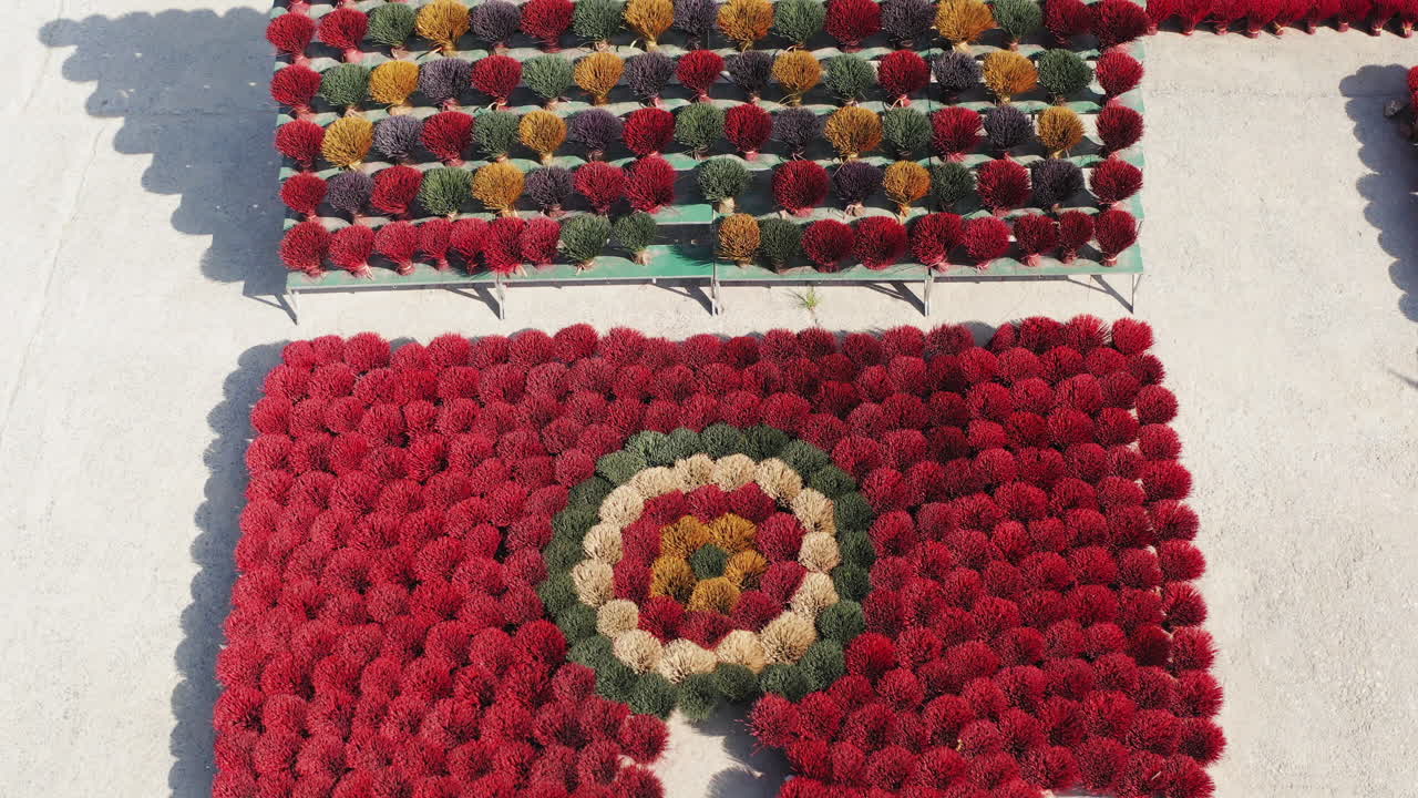 A drone reveals the incense drying square in Quang Phu Cau Village, Ha Noi, Vietnam, where bundles in red, yellow, green, and black form symbolic and geometric patterns across the courtyard.