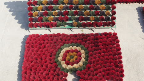 a drone reveals the incense drying square in quang phu cau village, ha noi, vietnam, where bundles in red, yellow, green, and black form symbolic and geometric patterns across the courtyard.