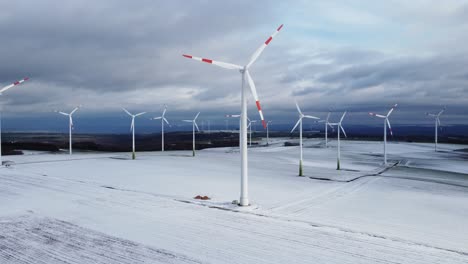 aerial backwards shot of rotating wind turbine farm in winter with snow covered and frozen agricultural fields