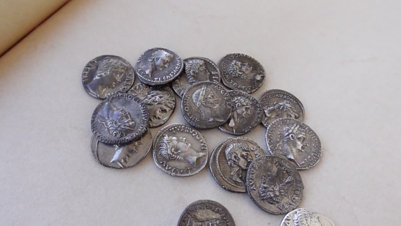 Antiguas monedas romanas de plata cayendo sobre un fondo neutro.