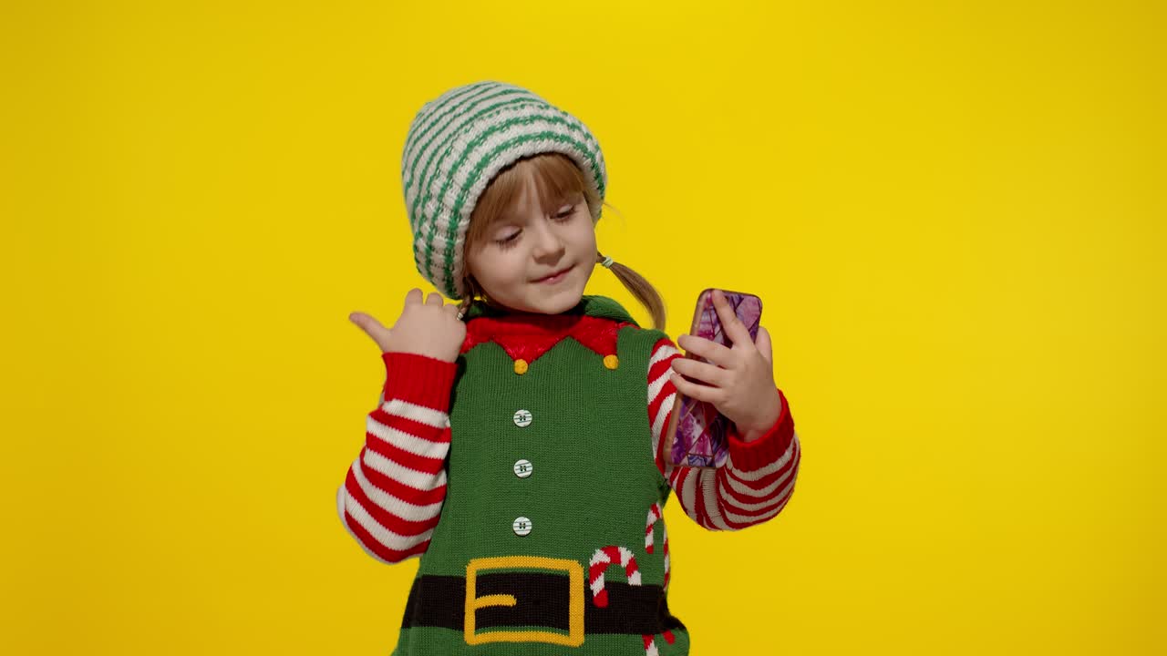 Holčička v kostýmu vánočního skřítka uskutečňuje videohovor na mobilním telefonu.
