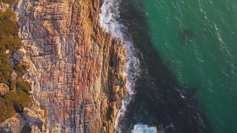 Blick-Von-Oben-Nach-Unten-Auf-Wellen,-Die-Bei-Sonnenaufgang-Mit-Sanftem-Morgenlicht-An-Der-Felsigen-Küste-In-Westaustralien-Zusammenbrechen