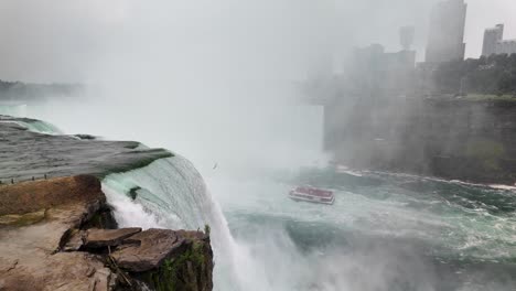 view of a tourist boat sailing at the foot of niagara falls with fog and powerful rapid water. view of a tourist boat sailing at the foot of niagara falls with fog and powerful rapid water