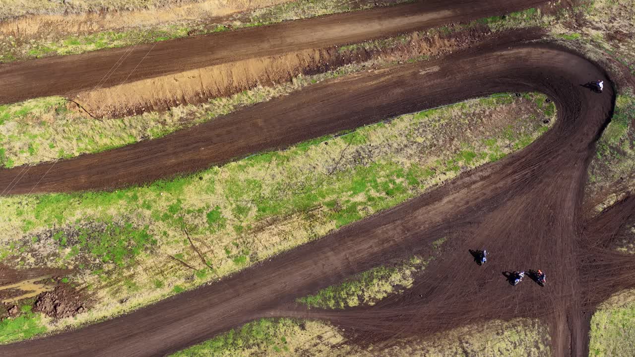 Motorbikes race on winding dirt track through bushland