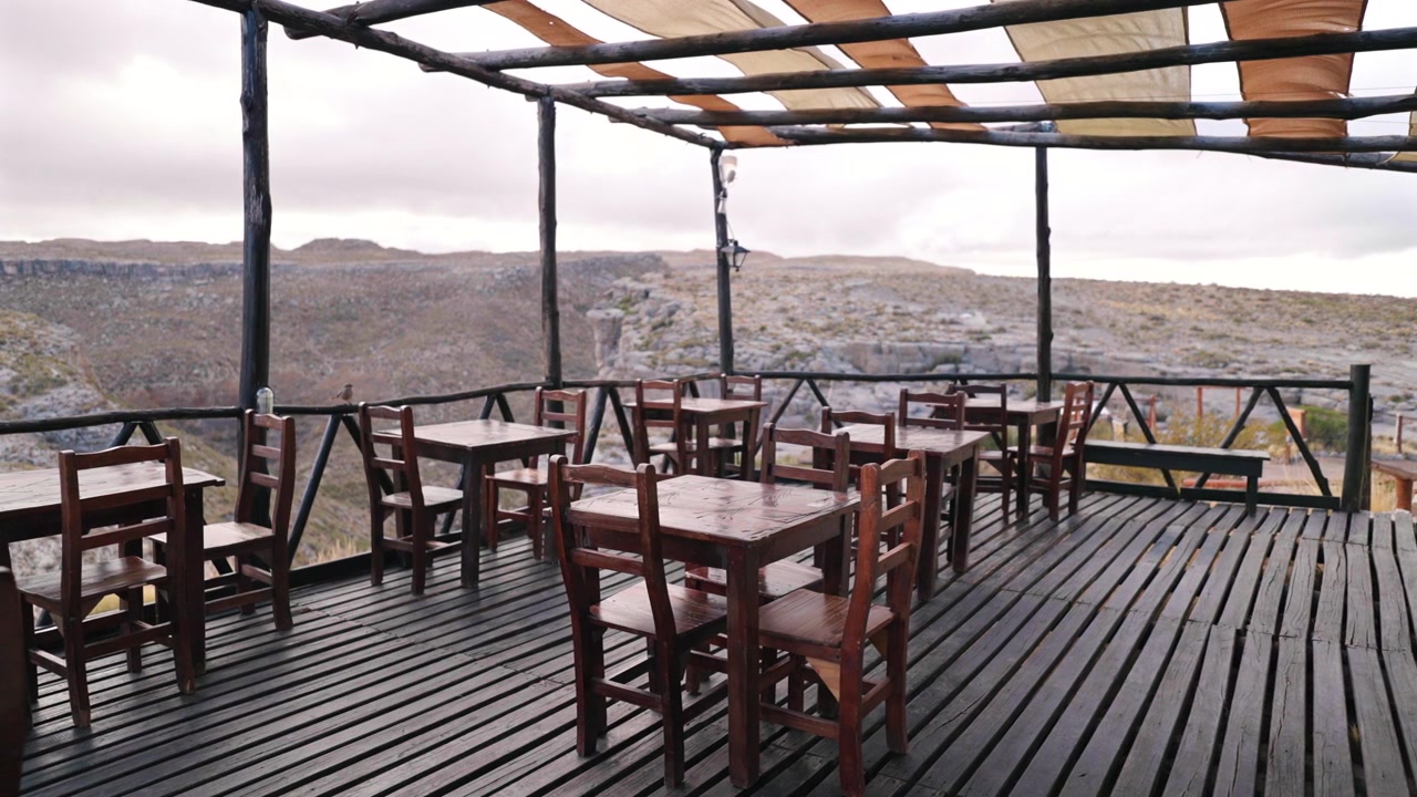 Restaurantterrasse im Freien mit Holzdeck und Blick auf eine dramatische Anden-Berglandschaft.