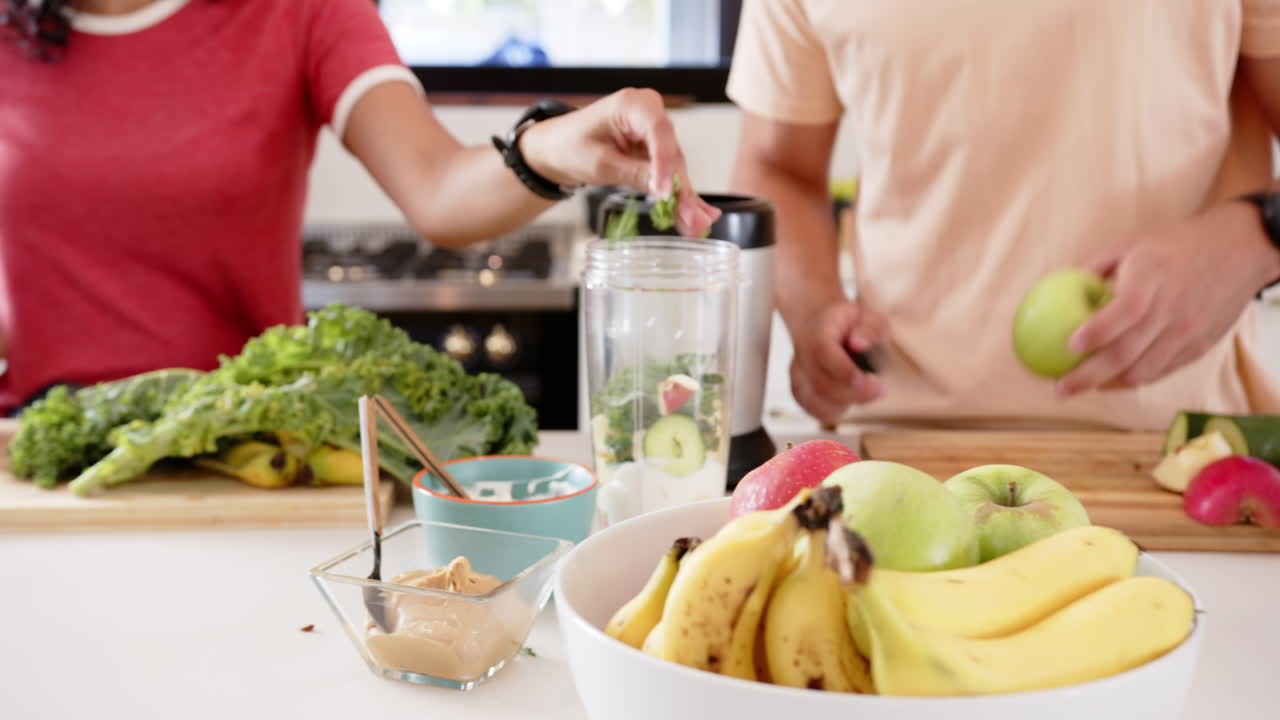 Preparing healthy smoothie, young multiracial couple chopping fruits and vegetables, at home
