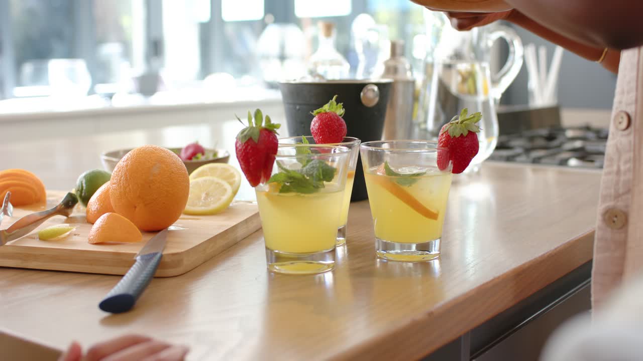 African American man bringing mint, pinching into two drinks with strawberries on counter to serve