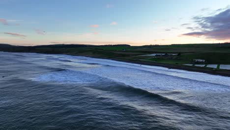 Dunbar's-Ocean-Canvas-Aerial:-Surfers-on-the-Scottish-Coast-at-Thorntonloch-Beach,-Scottish-Beach-at-Sunset,-Scotland,-United-Kingdom