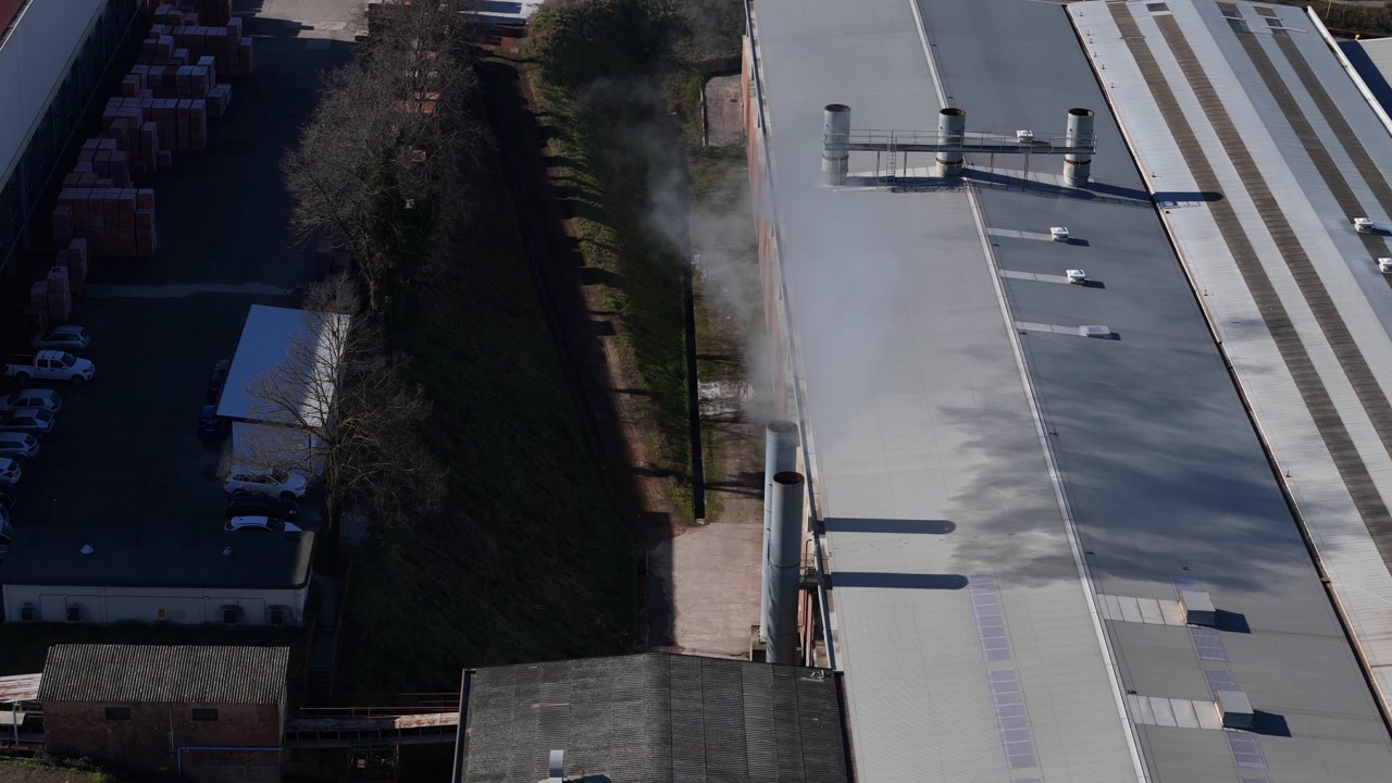 Drone captures an industrial facility with smoke emerging from large chimneys on the rooftop, showcasing manufacturing operations from above