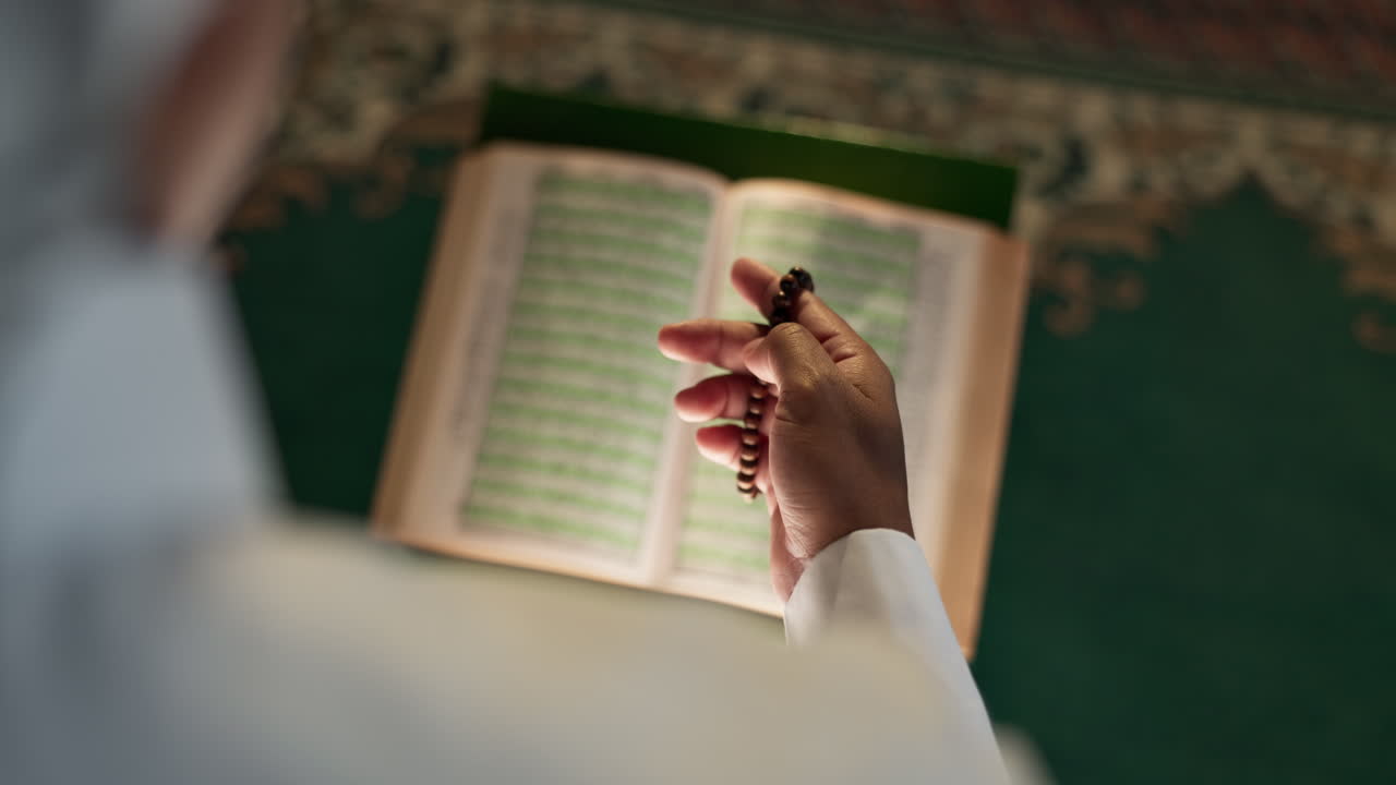 Una persona che legge il Corano con un rosario in mano