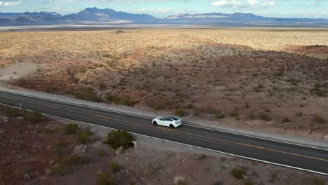 cinematic aerial zoom in of a modern white electric vehicle traveling on empty road on a sunny day in nevada