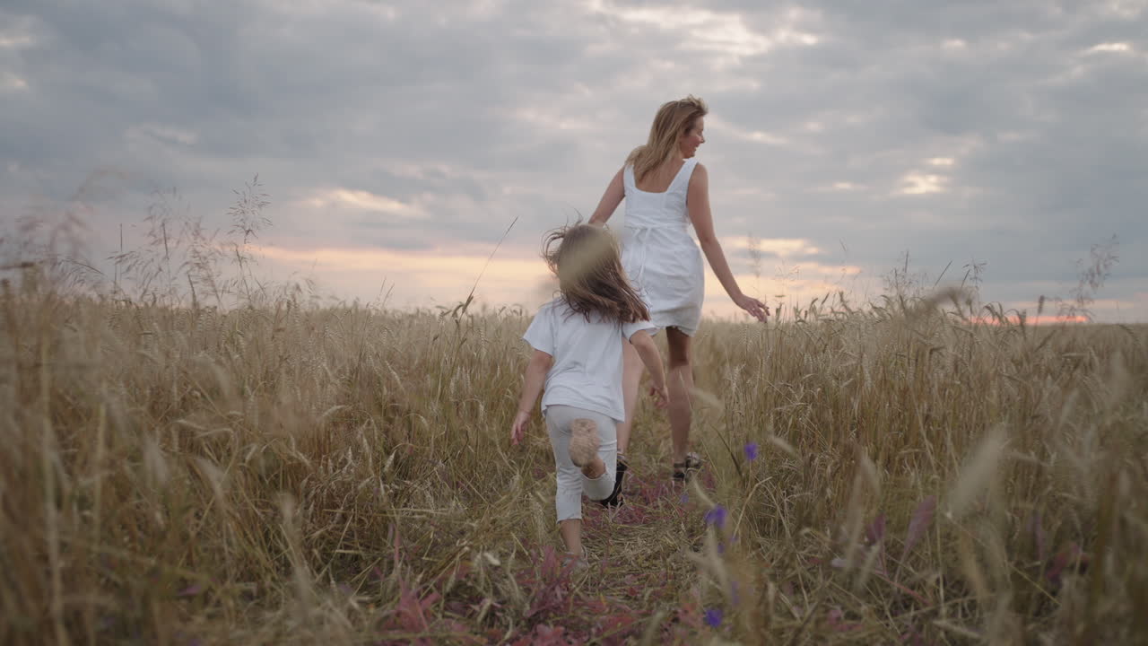 la hija y la madre sueñan juntas corriendo en el campo de trigo al atardecer. gente de familia feliz en el concepto del campo de trigo. mamá y niña jugando a correr. niño divertido corriendo en un prado verde.