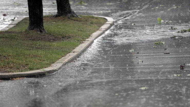 Heavy rain in slow motion, water accumulating along curb of grassy sidewalk