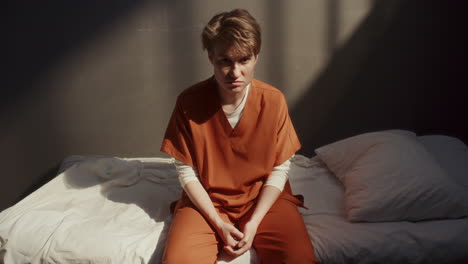 portrait of female prisoner sitting on bed, staring seriously at camera