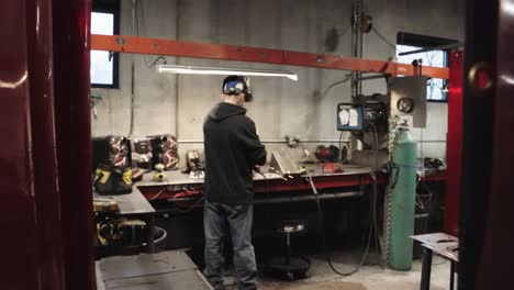 back of blue collar worker grinding metal with hand held saw in workshop, slow motion