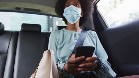 mujer de negocios afroamericana con máscara facial usando un teléfono inteligente