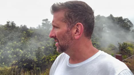 Male-walking-near-Mauna-Loa-volcano-in-Hawaiian-National-Park,-sulfur-smoke-rising-between-foliage-trees