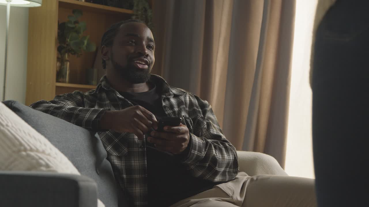 mujer sentada al lado de un hombre en el sofá en casa usando teléfono móvil y hablando