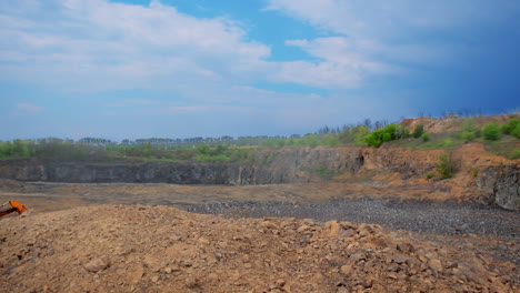 Construction site with heaps of sand and stones. Wasteland for building. Piles of soil surrounded by nature. Excavator works on the ground.
