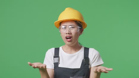 close up of wondering asian woman worker wearing goggles and safety helmet saying why and standing doubtfully in the green screen background studio