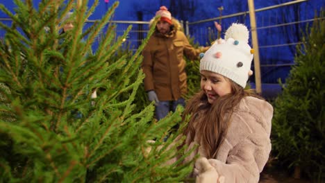 Glückliche-Familie-Kauft-Weihnachtsbaum-Auf-Dem-Markt.Familie,-Winterferien-Und-Menschenkonzept-–-Glückliche-Mutter,-Vater-Und-Kleine-Tochter-Kaufen-Weihnachtsbaum-Auf-Dem-Straßenmarkt-Am-Abend-Bei-Fallendem-Schnee