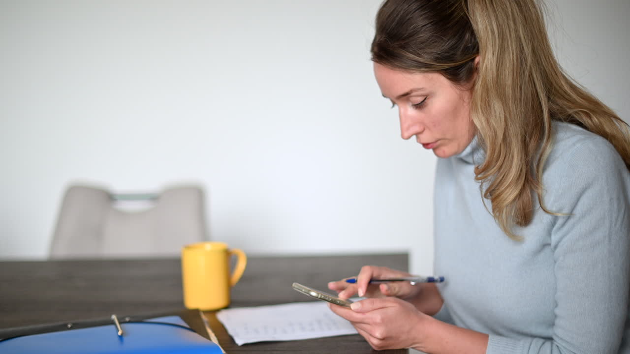 Woman working on mobile phone and writing at the office