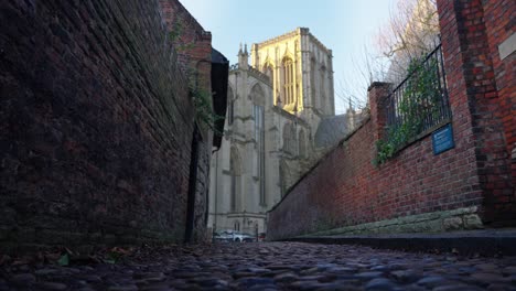 Side-movement-of-large-cathedral-from-low-angle-on-cobbled-alley-way-in-historic-city-of-York