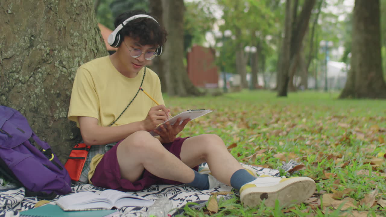 Asian Student in Headphones Doing Homework in Park