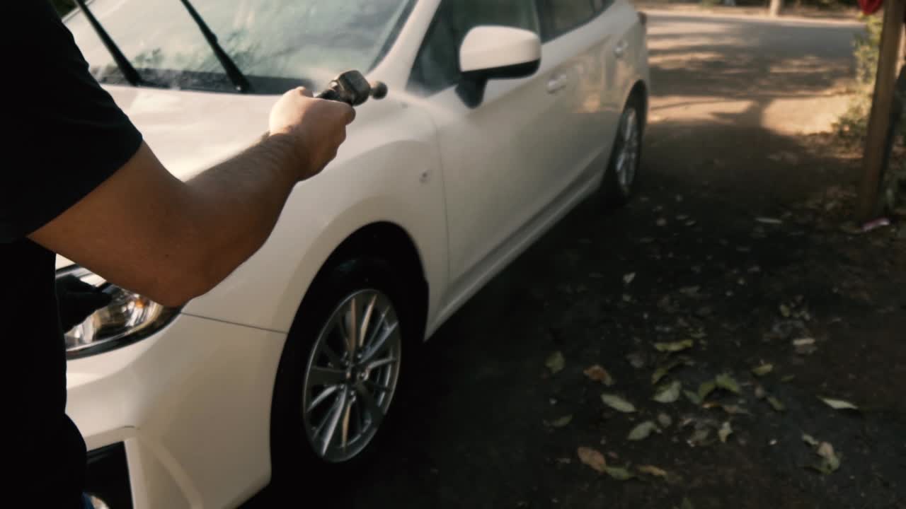 hombre limpiando un auto blanco con una lavadora a presión