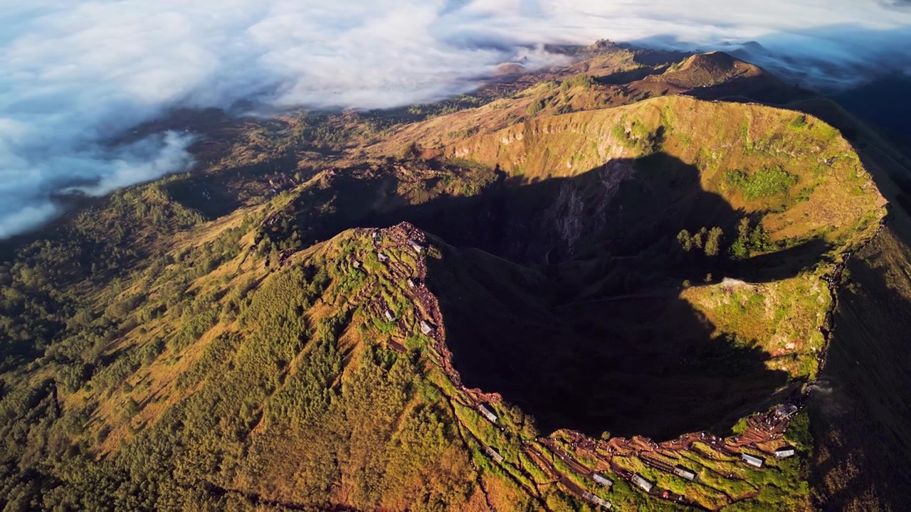 Trilha de caminhada do Monte Batur ao longo da crista da cratera vulcânica com caminhantes em trilha estreita e vistas panorâmicas sob a luz quente da manhã, com encostas dramáticas e sombras da caldeira capturadas em filmagem aérea de drone.