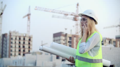 dialogue on the phone a woman in a helmet on the background of construction discusses with the director of the construction site of the building.