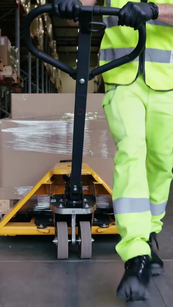 Video verticale: Inquadratura bassa iniziale di un lavoratore in abbigliamento ad alta visibilità che guida un transpallet lungo il corridoio, spostando scatole.